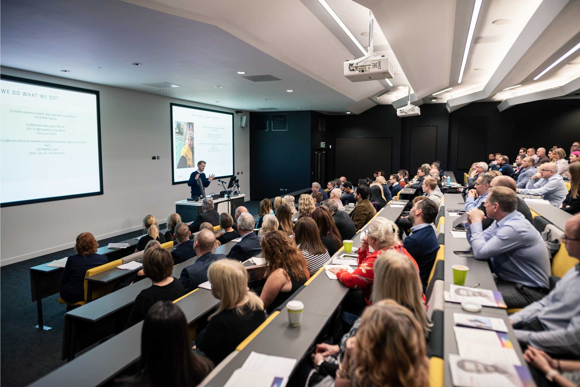 Many people sat in a room listening to a speaker