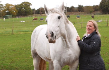 Lady pictured smiling with her horse on a field