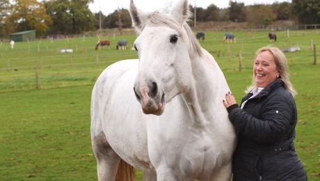 Lady pictured smiling with her horse on a field