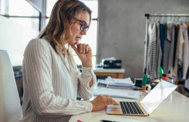 Lady scrolling through her laptop on her desk by a rack of clothes