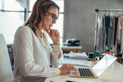 Lady scrolling through her laptop on her desk by a rack of clothes