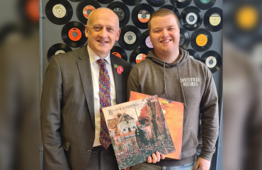 Vinyl music shop owner in front of decorative vinyl's on the wall