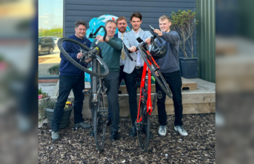 Group of gentleman holding 2 bikes, one black, one red, in front of decking