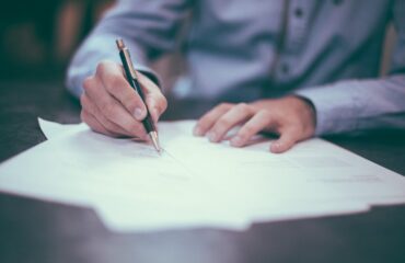 Gentleman writing on a piece of paper, wearing a blue shirt