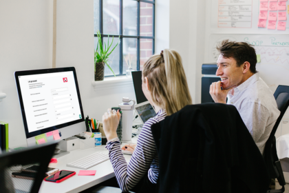 A man and a women looking at their laptop, while sat in front of a wall with sticky notes on