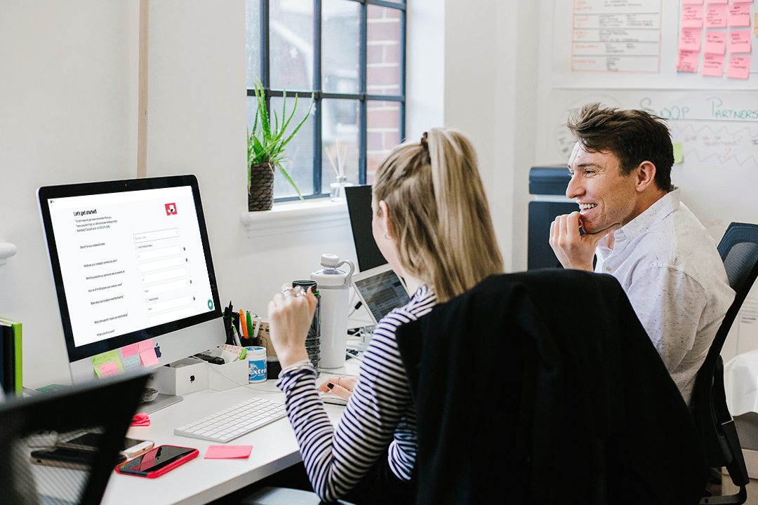 A man and a women looking at their laptop, while sat in front of a wall with sticky notes on