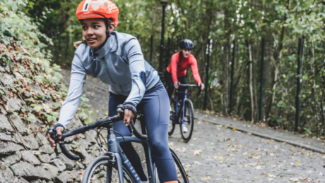 Two women riding a bike down a track with trees and other rocks at the side