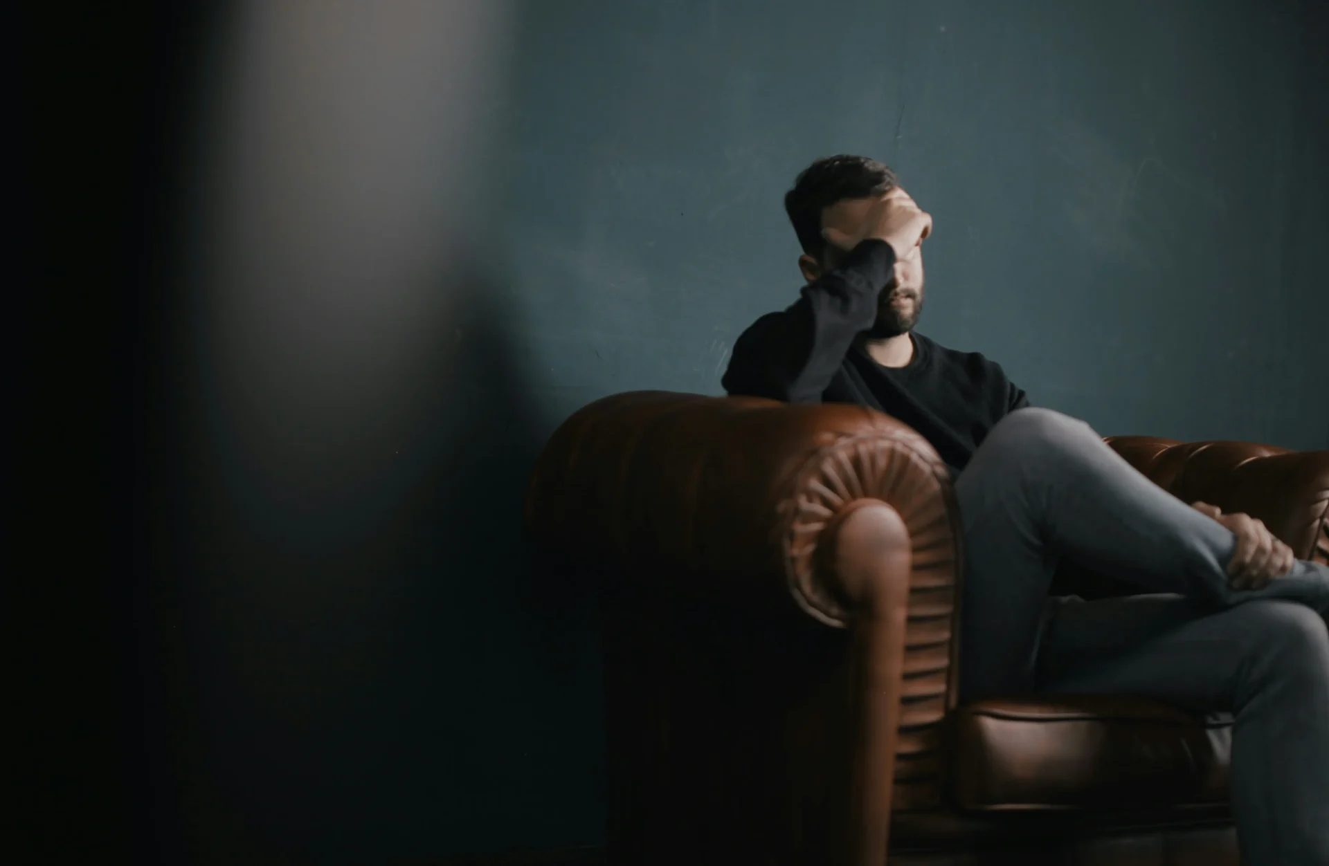 Picture of someone who has his hand on his forehead and on a couch stressed.