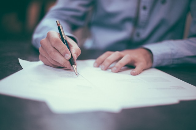 Manin blue suit writing on a piece of paper using his right hand.