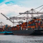Cargo ships loaded with colorful shipping containers docked at a port with large white cranes and SSA Terminals signage.