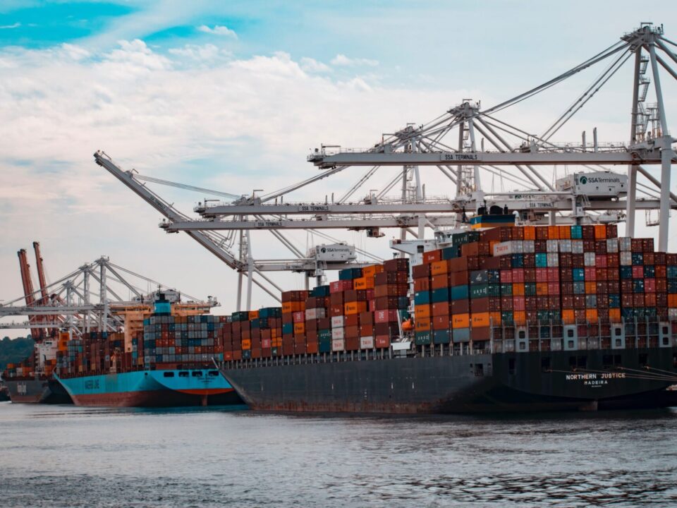 Cargo ships loaded with colorful shipping containers docked at a port with large white cranes and SSA Terminals signage.