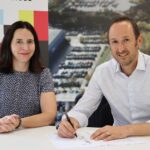 A picture of two people at a table and one is signing a document