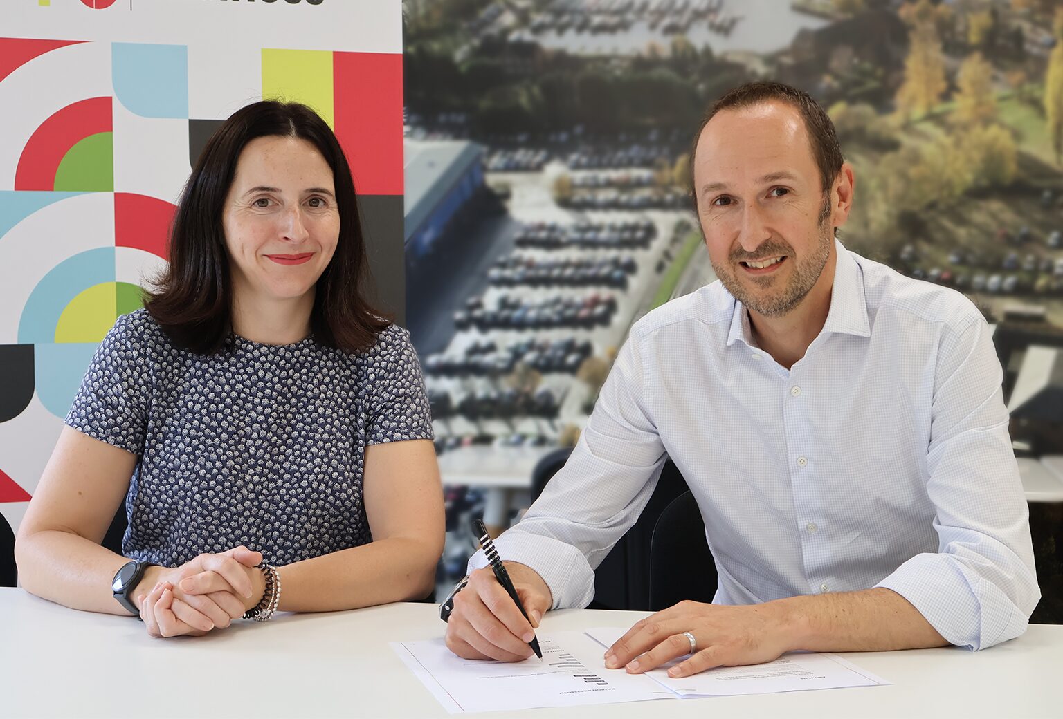 A picture of two people at a table and one is signing a document