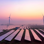 Picture of a solar panel farm with some wind turbines behind them.