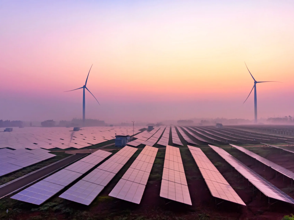 Picture of a solar panel farm with some wind turbines behind them.
