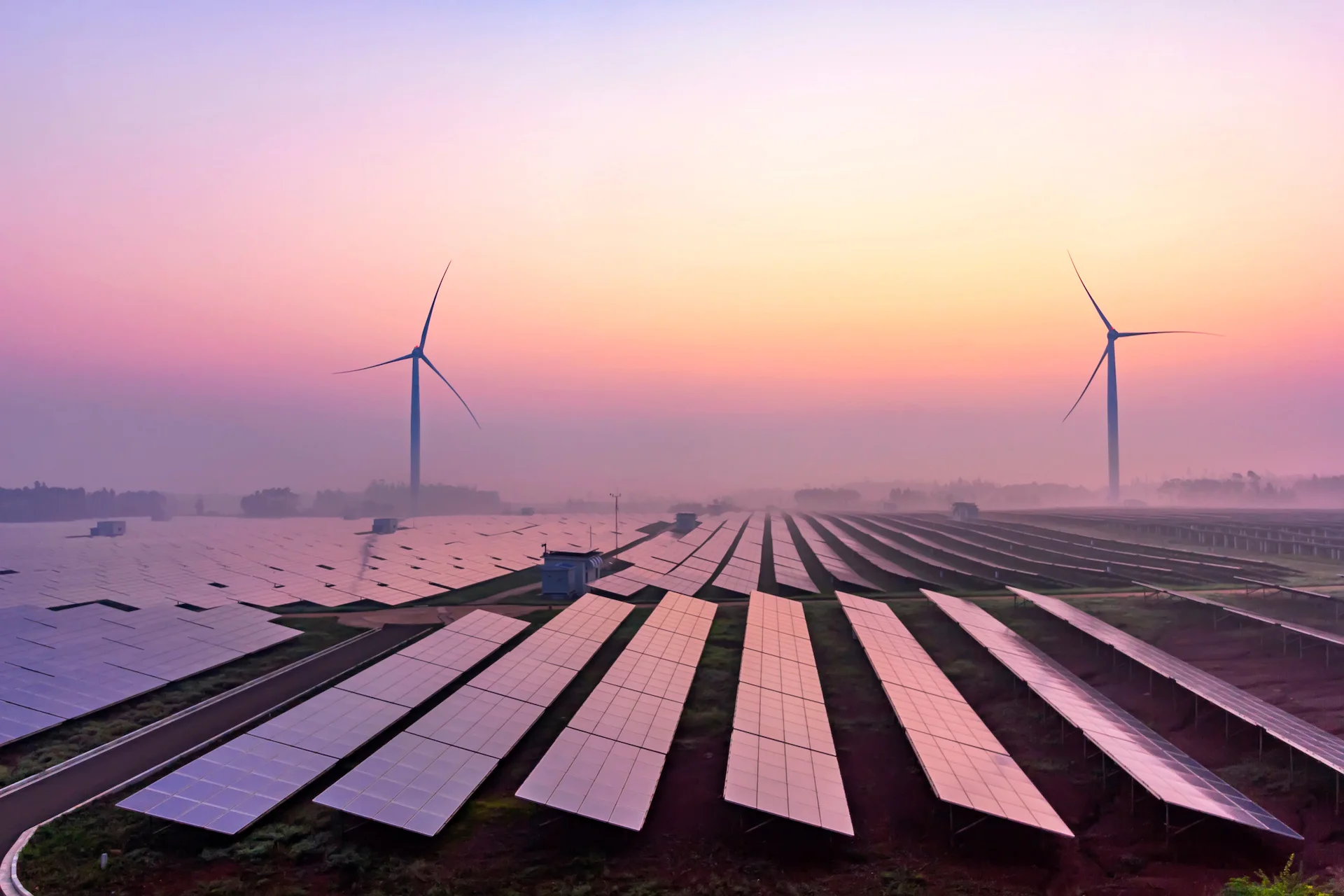 Picture of a solar panel farm with some wind turbines behind them.