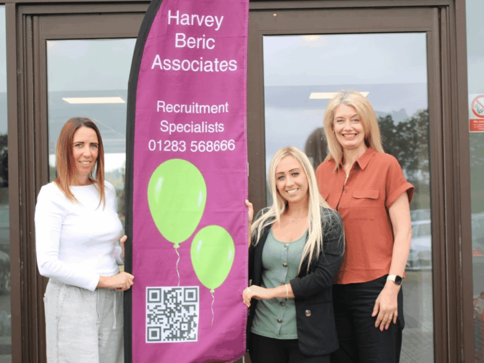 People from Harvey Beric Associates standing next to a banner. Supporting local employers and candidates.