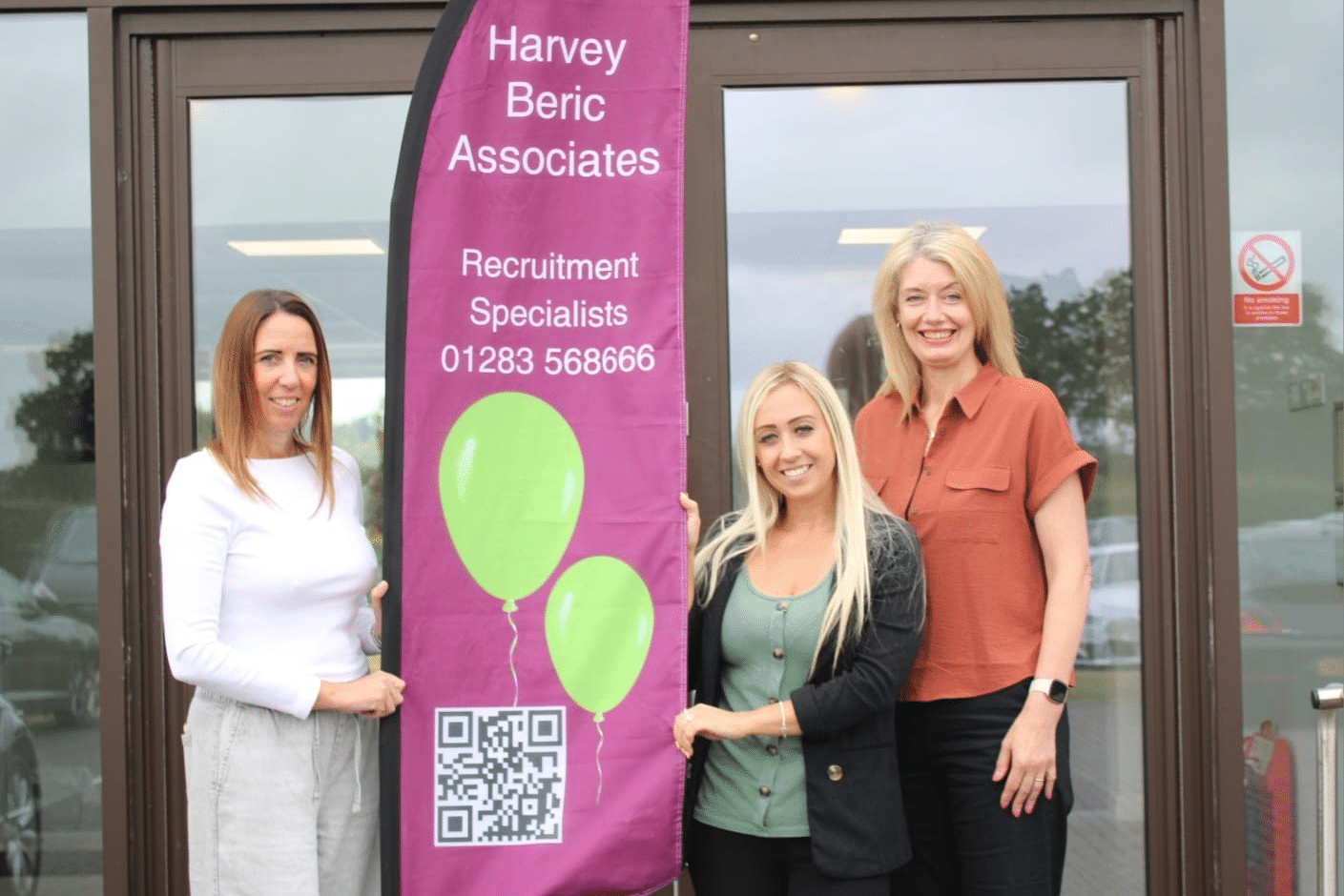 People from Harvey Beric Associates standing next to a banner. Supporting local employers and candidates.