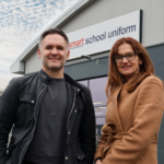1 person from smart school uniform and another from Staffordshire chambers of commerce stood Infront of smart school uniform building.