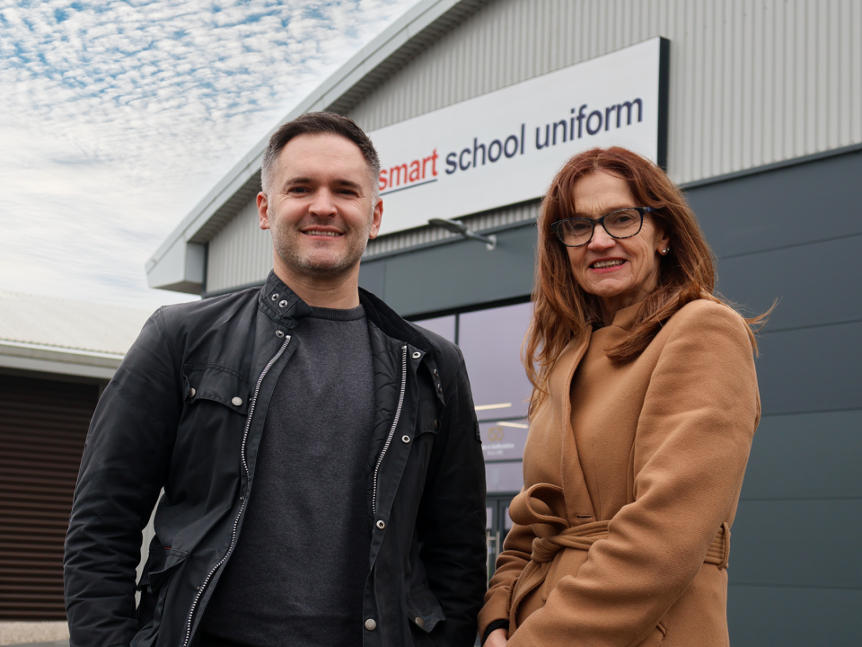 1 person from smart school uniform and another from Staffordshire chambers of commerce stood Infront of smart school uniform building.
