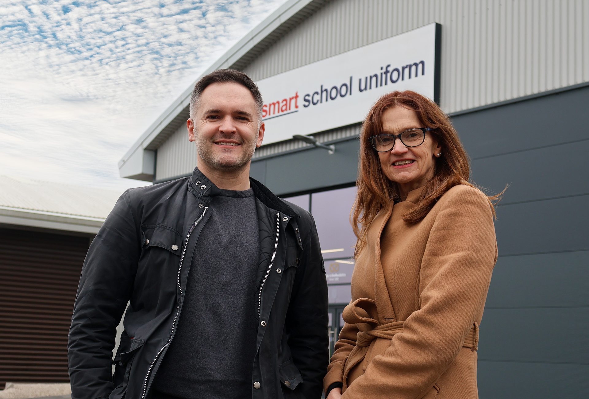 1 person from smart school uniform and another from Staffordshire chambers of commerce stood Infront of smart school uniform building.