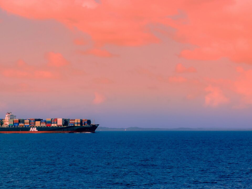 Picture of a cargo ship in the middle of the sea at sunset.