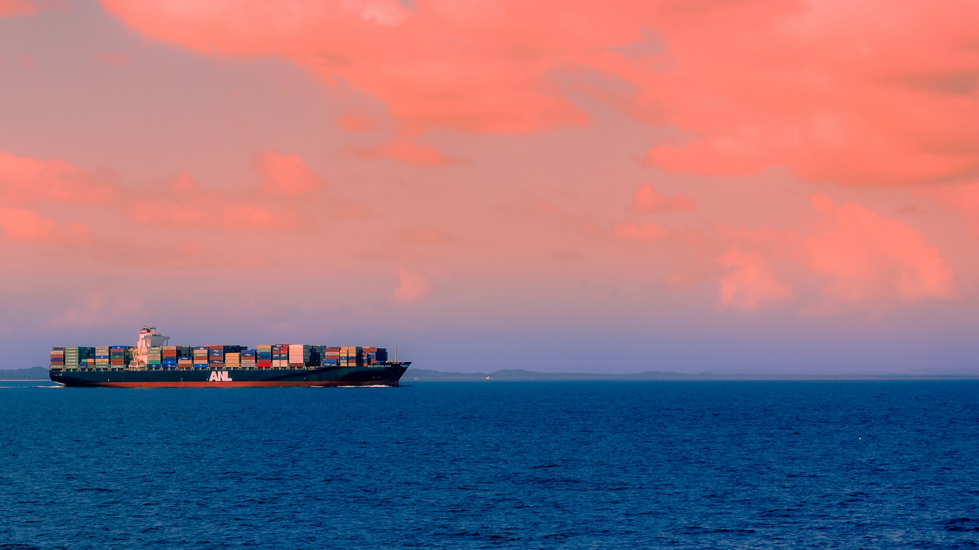Picture of a cargo ship in the middle of the sea at sunset.